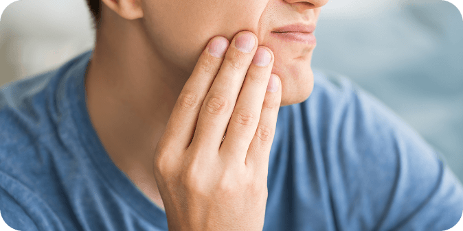 Man holding the side of his mouth, with a pained look on his face. 