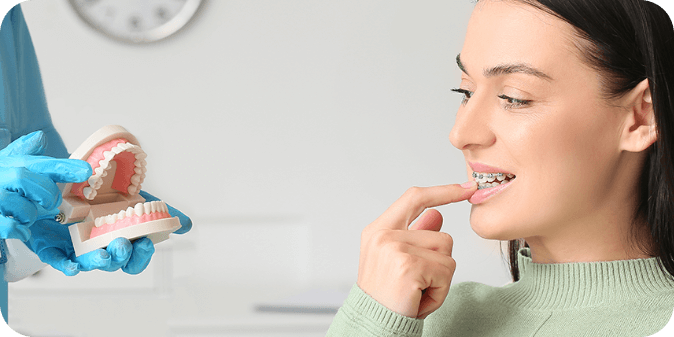 A lady wearing braces at the dentist learning about her teeth using a model of teeth and jaws.