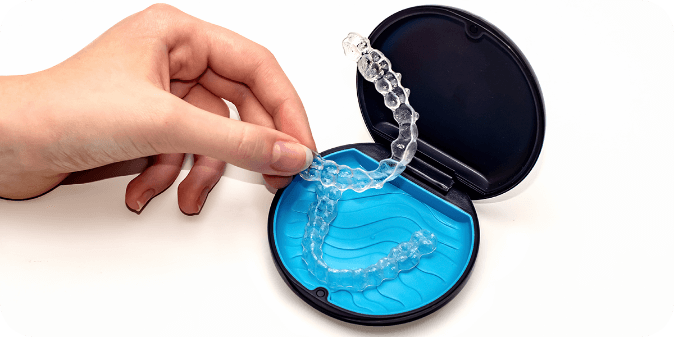 Hands picking up Invisalign / clear aligners and an aligner case.
